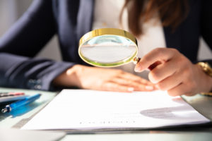 Close-up Of A Businesswoman's Hand Looking At Contract Form Through Magnifying Glass
