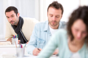 View of a Classmate in the background trying to cheat of students seated ahead of him.