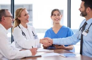 Group of doctors shaking hands after signing a physician contract.